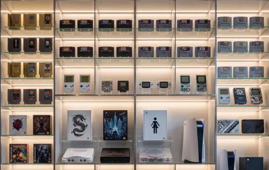 Uma estante moderna e bem iluminada exibindo uma coleção impressionante de consoles clássicos, portáteis e de nova geração, perfeitamente organizados para celebrar os games épicos que definem a cultura nerd e gamer em nosso acervo.